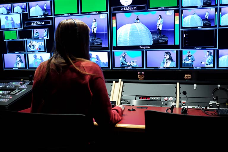 A student wearing headphones looks at multiple screens in a Radio-Television Building studio.
