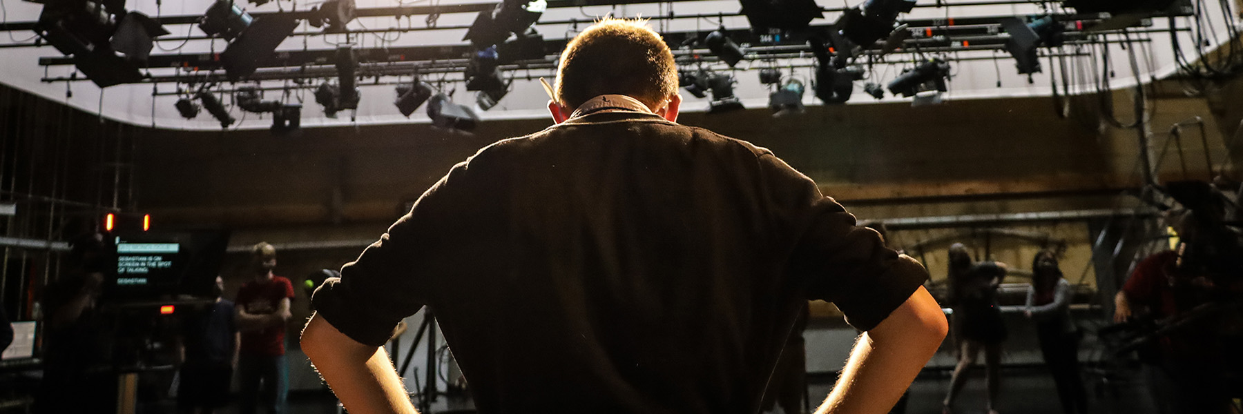 Man standing on stage with lights and with back to camera. 