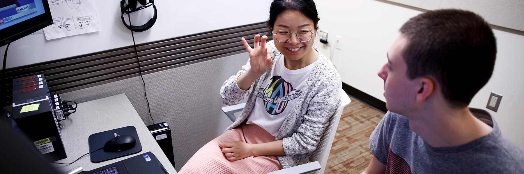 Two students researchers chat at a computer desk.