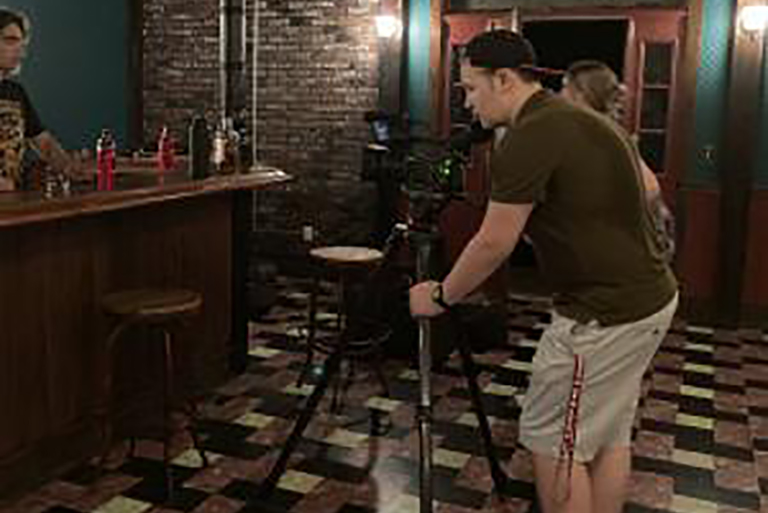 A student stands with a camera in a mock studio in the Radio-Television Building.