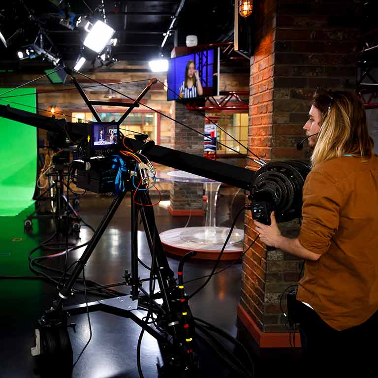 A student operates a large camera on a TV set.