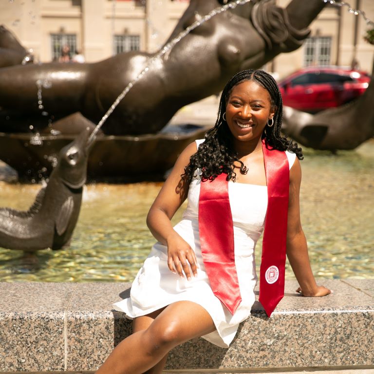 Person wearing a graduation stole sits next to the Showalter Fountain. 