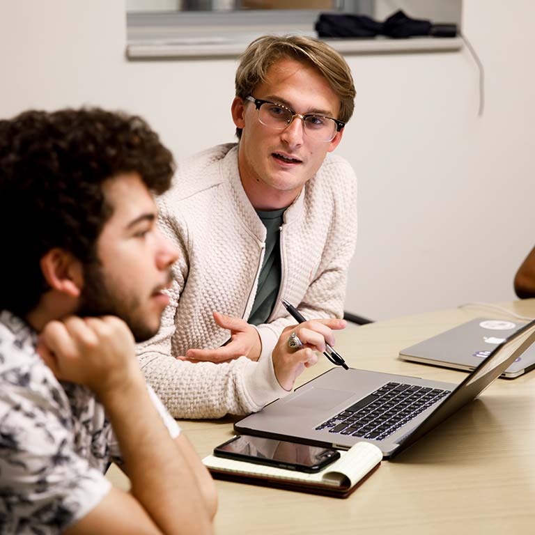 Two students seated at a table take part in a discussion.