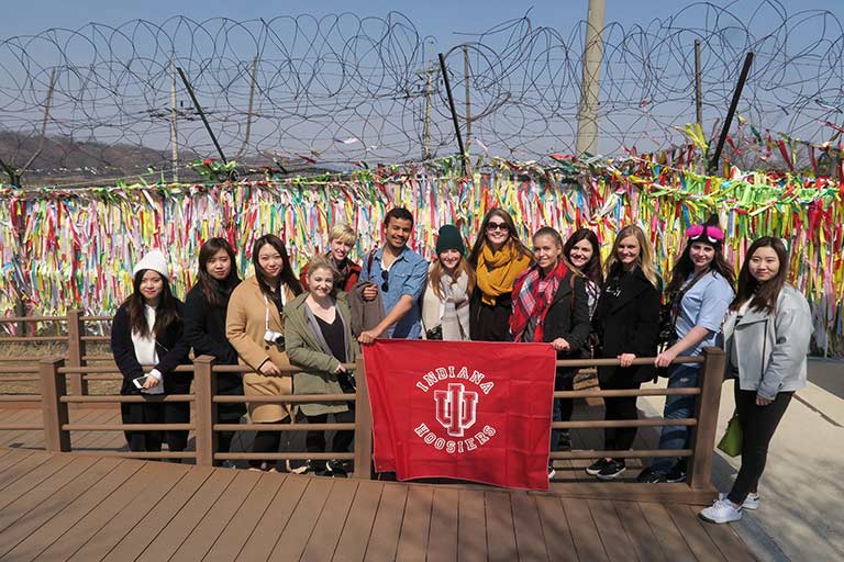 A group of students pose behind an Indiana Hoosiers flag.
